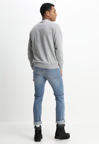 Felpa grigia in cotone con polsini a coste, abbinata a jeans di denim blu e stivali neri con lacci. Modello mostrato di spalle.
