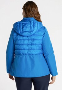 Chaqueta de plumas azul con capucha, textura acolchada y cintura ceñida. La tela parece brillante con un diseño suave y ligero.