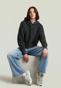 Felpa nera cropped in tessuto testurizzato, con cappuccio e cuciture visibili. Abbinata a jeans svasati di colore blu chiaro e sneakers bianche chunky.