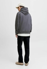 Sudadera gris con capucha, de corte relajado, con dobladillo y puños de canalé, combinada con pantalones negros y zapatos beige, vista desde la parte posterior.