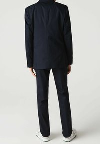 Marinblå kostym med skräddarsydd passform, enkel ventil bak, och långa ärmar, ihop parat med vita sneakers. Slät textur, minimala dekorationer.