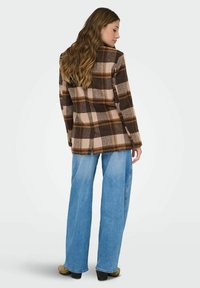 Chaqueta de mezcla de lana en cuadros marrón y beige, con solapa, abertura trasera y mangas largas, combinada con pantalones de mezclilla de pierna ancha en azul claro.