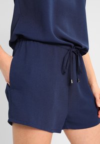 Shorts bleu marine en tissu léger, dotés d'une taille élastique avec un cordon de serrage et des embouts en métal argenté. Poches latérales incluses.