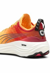 Zapatillas deportivas con una parte superior de malla en un degradado de naranja a rojo, acentos metálicos en plata y una suela acolchada blanca con detalles en negro y rojo.