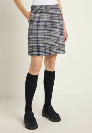 Plaid skirt in brown, blue, and white; knee-length with pockets and a fitted waist. Paired with knee-length black socks and loafers.