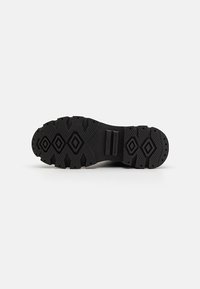 Suela de zapato de goma negra con un diseño de banda de rodadura que presenta formas de diamante y crestas elevadas para mayor tracción. Secciones lisas con dos hendiduras rectangulares.