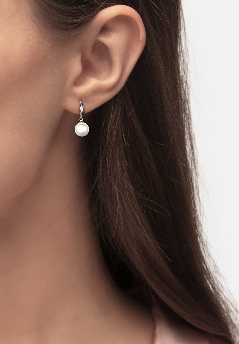 Gros plan sur l’oreille d’une femme portant une boucle d’oreille créole en argent avec un pendentif unique en perle blanche ronde suspendu.