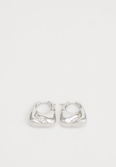 Boucles d'oreilles en argent en forme de créoles lisses et arrondies, avec un accent ondulé et de petits strass transparents le long d'un bord.