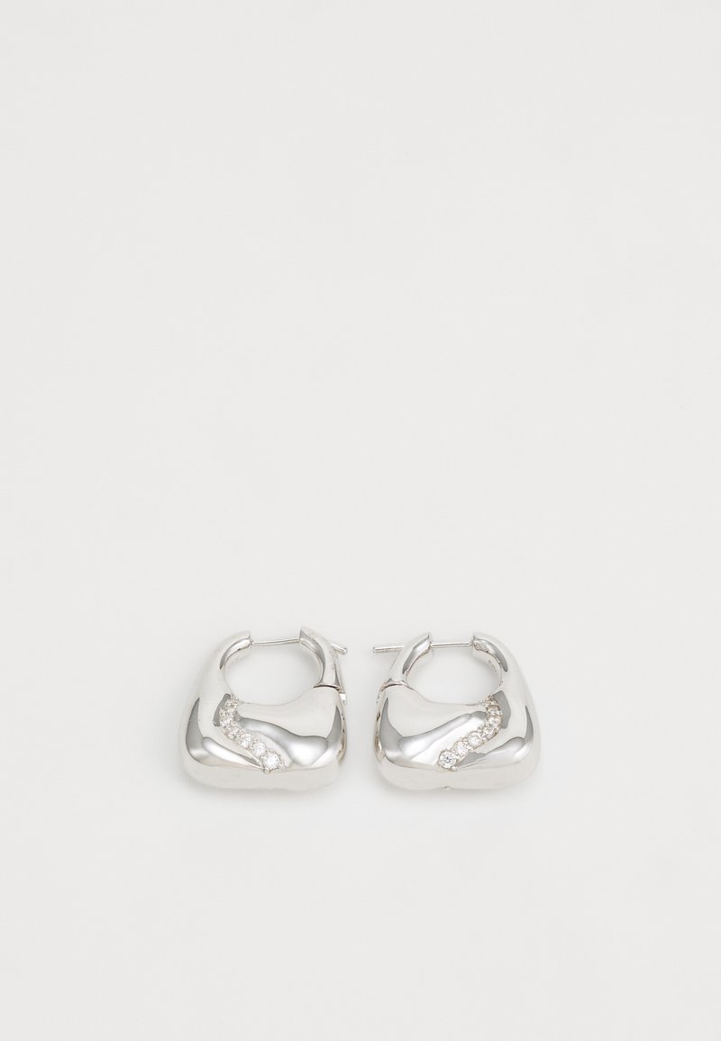 Brincos de argola prateados com um design liso e arredondado, apresentando um detalhe ondulado com pequenos strass transparentes ao longo de uma das bordas.