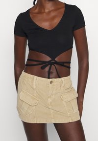 Top corto negro de manga corta con escote en V profundo y detalles de lazo. Falda mini de pana beige con dos bolsillos laterales en la parte delantera y cintura elástica.