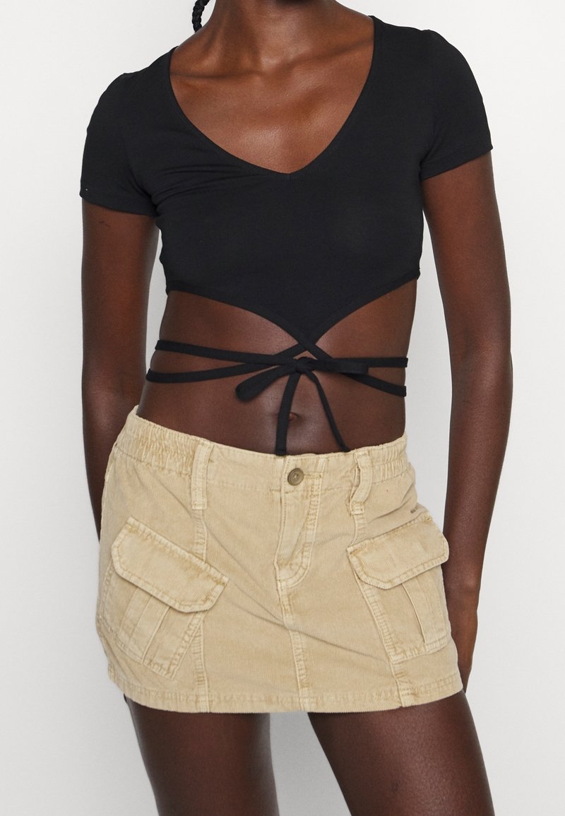 Top corto negro de manga corta con escote en V profundo y detalles de lazo. Falda mini de pana beige con dos bolsillos laterales en la parte delantera y cintura elástica.
