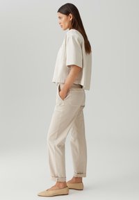 Camicia cropped beige con maniche corte, abbinata a pantaloni leggermente beige arrotolati e ballerine beige, con un design semplice e minimal.