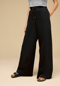 Pantaloni negri cu picior larg, cu talie elastică și șnur. Textură moale a materialului, cu buzunare laterale, asortați cu sandale negre.