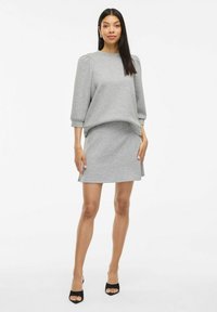 Sweatshirt gris avec un col rond et des manches bouffantes 3/4, associé à une jupe mini grise assortie. Tissu lisse, design décontracté.