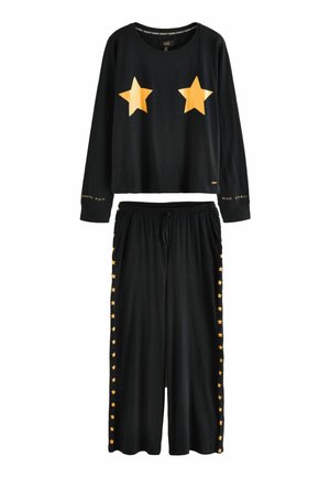Schwarzes Loungewear-Set mit einem verkürzten Langarmtop, das zwei orangefarbene Sterne aufweist, und einer lockeren Hose, die an den Seiten mit orangen Sternmustern akzentuiert ist.