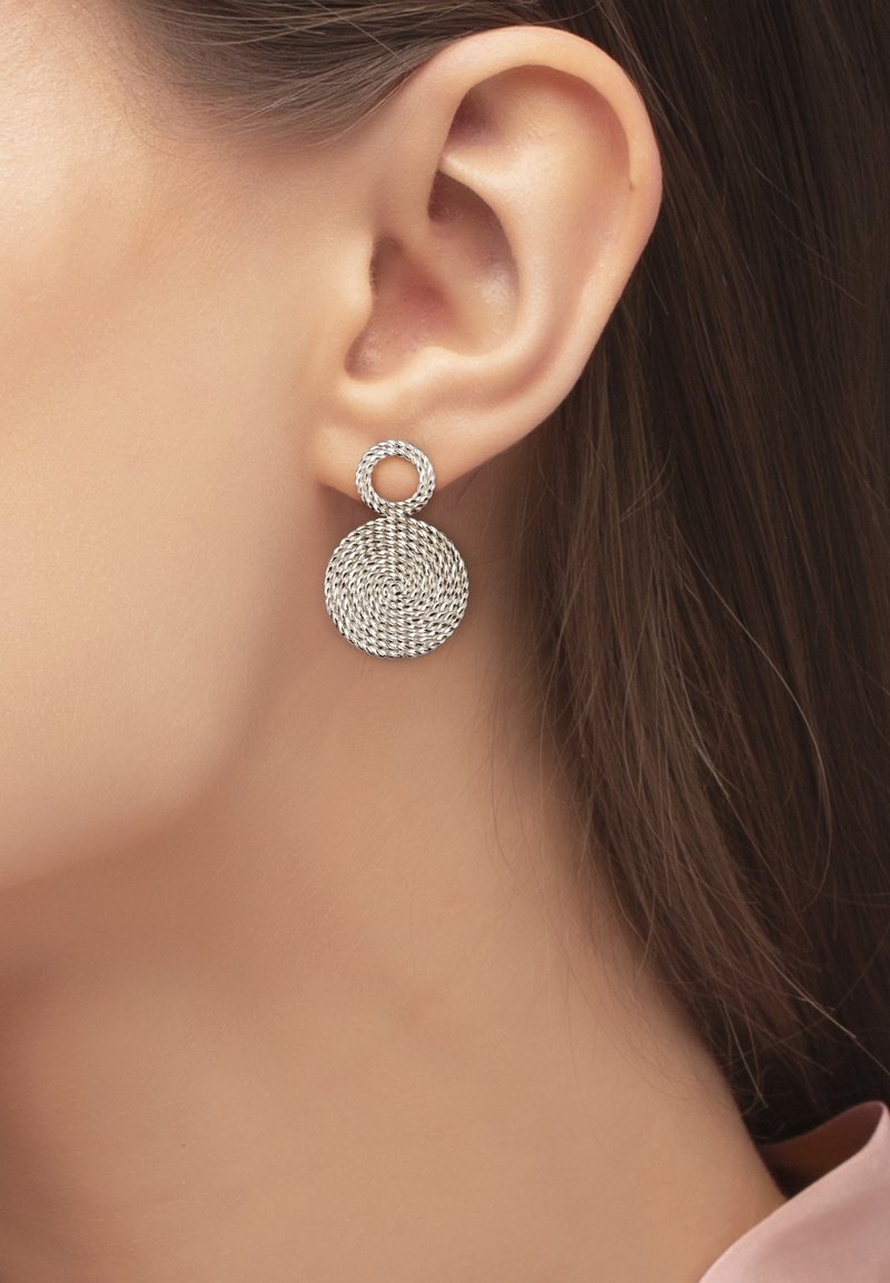 Gros plan sur l'oreille d'une femme portant une boucle d'oreille en argent au design de corde torsadée avec un petit cercle au-dessus d'un cercle plus grand.