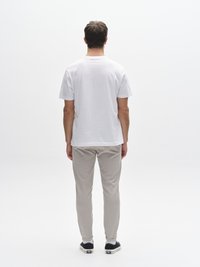 Vit bomulls-t-shirt med korta ärmar, matchad med ljusgrå koniska byxor med elastiska muddar och svarta sneakers.