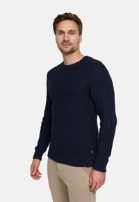 Marineblauw ribgebreid sweater met een ronde hals en lange mouwen; voorzien van een textuurpatroon en een klein logo-label onderaan.