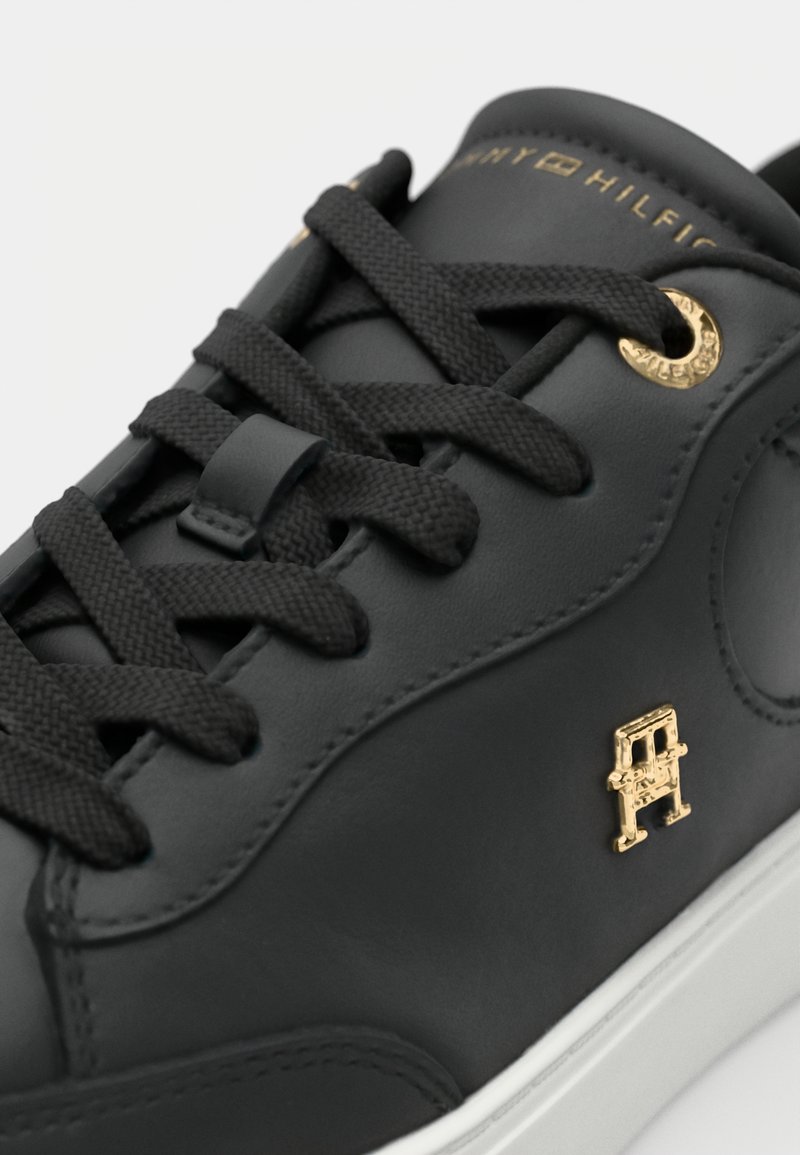 Sneaker in pelle nera con accenti dorati, lacci texture e suola bianca. Presenta un particolare dettaglio in hardware dorato sul lato.