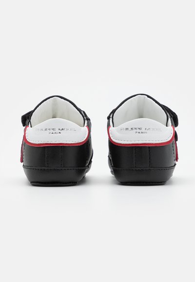 Sapatos de couro pretos com um destaque em branco e vermelho, apresentando uma forma arredondada, forro macio e detalhe de marca na parte traseira.