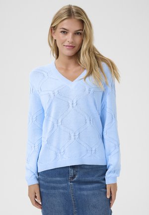 Hellblaues gestricktes Sweatshirt mit V-Ausschnitt, ziert ein Rautenmuster, gerippte Bündchen und Saum. Eine Kombination mit einem Jeansrock ist sichtbar.