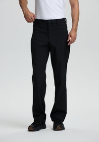 Pantalones negros de corte relajado, con una textura suave, bolsillos frontales y un diseño sutil. Combinados con zapatillas negras.