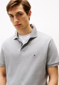 Polo gris en tissu doux, avec col, patte de boutonnage à trois boutons et petit logo sur la poitrine gauche.