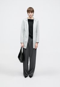 Világosszürke blézer, fekete felső és bő szürke nadrág. A modell egy fényes fekete kézitáskát tart. Karcsúsított szabás, sima textúra, minimalista dizájn.