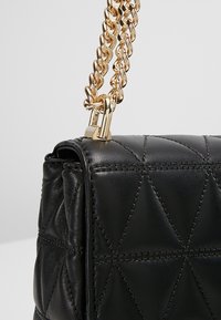 Černá kožená kabelka s prošívaným geometrickým vzorem, zlatým řetízkovým popruhem a kovovou sponou. Hladká textura.