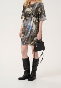 Tiskované šaty s krátkým rukávem v modrých a černých abstraktních vzorech, doplněné černými koženými holínkami do kolen a malou texturovanou černou kabelkou.