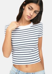 Bílý crop top s námořnickými vodorovnými pruhy, ribbovanou texturou a krátkými rukávy, kombinovaný s volnými džínovými šortkami.