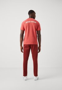 Röd sportt-shirt med "BAYERN MÜNCHEN" tryckt på ryggen, matchad med röda träningsbyxor med sidostreck och vita sportskor.