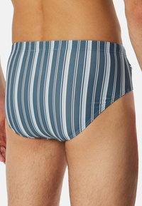 Randiga baddräktsbyxor i nyanser av blått med vertikala vita ränder. Tillverkade av ett slätt, stretchigt material med en åtsittande design och låg midja.