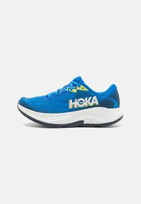 Blauwe sportieve schoen met een bovenwerk van mesh, gele accenten, dikke witte zool en een gestructureerd ontwerp. Beschikt over veters en een merklogo op de zijkant.