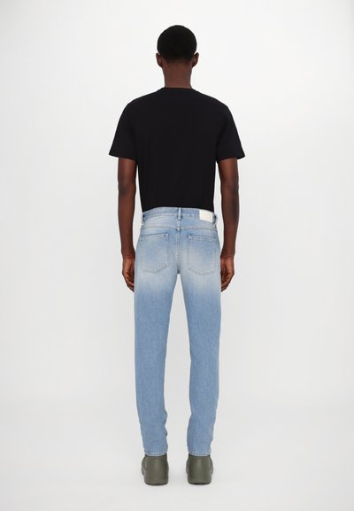 Jean en denim bleu clair délavé à coupe droite, associé à un t-shirt noir uni, vu de dos. Design minimaliste et branding subtil.
