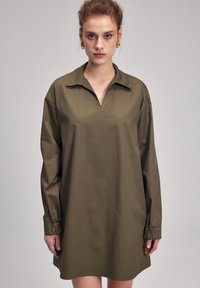 Robe chemise oversize vert olive avec un col, des manches longues à poignets froncés et un design épuré et minimaliste.