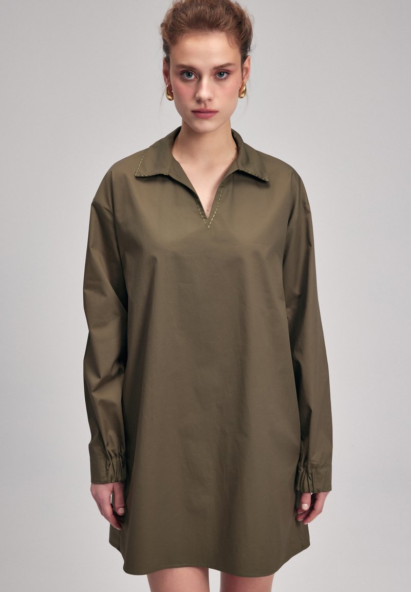 Olivově zelené oversized košilové šaty s límečkem, dlouhými rukávy se staženými manžetami a čistým, minimalistickým designem.
