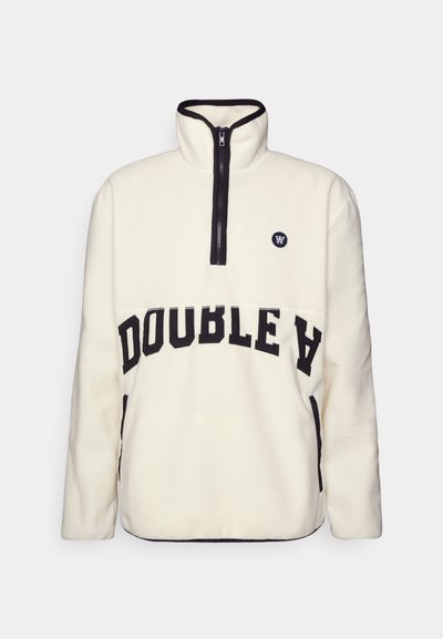 Quarter-zip fleece genser i krem med svarte detaljer. Har "DOUBLE A" tekst i fet skrift, en rund logo på brystet, og sidelommer.