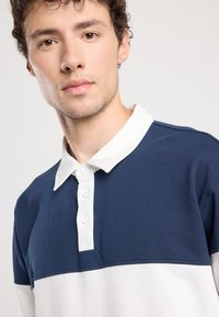 Navy and white polo shirt featuring a collared neck and a button placket, with a color-block design and soft cotton texture.