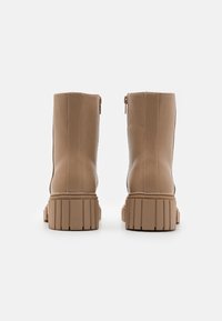 Botas de tobillo de imitación de cuero beige con una suela gruesa y estriada. Cierre de cremallera en la parte posterior y textura suave; sin patrones ni acentos visibles.