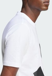 Witte katoenen t-shirt met een ronde halslijn en korte mouwen. Opvallend zwart grafisch ontwerp aan de voorkant. Soepele textuur.