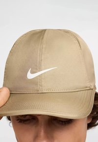 Cappellino Nike beige realizzato in tessuto morbido; presenta un logo bianco sulla parte frontale, dettagli cuciti e una visiera curva.