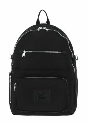 Sac à dos Lacoste noir avec plusieurs fermetures éclair argentées, patch logo à l'avant et sangles latérales ajustables, présenté sur fond blanc.