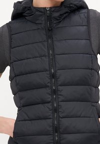 Svart ärmlös dunväst med huva, med horisontella vadderade sektioner, hel dragkedja framtill och matt yta.