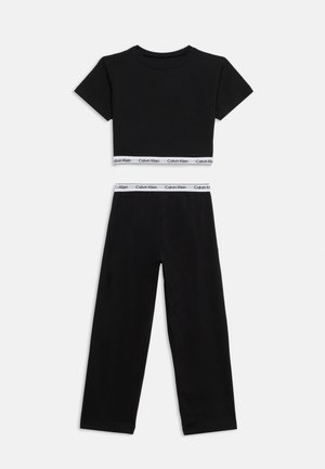 Zwart lounge-ensemble in twee delen met een korte mouw crop top en broek met wijde pijpen, beide voorzien van witte elastische banden met Calvin Klein-logo.