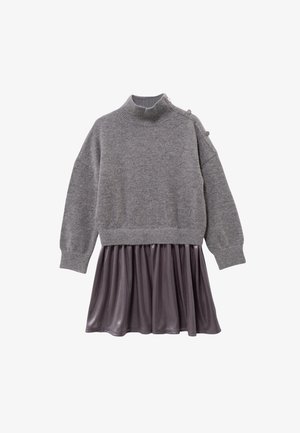 Suéter de punto gris con cuello alto y tres botones decorativos, combinado con una falda de satén gris oscuro y fluida. Manga larga.
