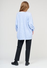 Hellblaues oversize Sweatshirt mit langen Ärmeln, gerippten Bündchen und Saum, kombiniert mit schwarzen gerade geschnittenen Hosen und schwarzen Ankle-Boots.