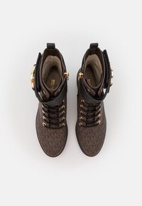 Hnědé členkové boty se vzorem vyrobené z kůže, se zlatým kováním, kulatou špičkou a šněrovacím designem. Obsahují dekorativní boční pásku.