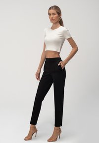 Bela skrajšana majica je kombinirana z črnimi krojenimi hlačami. Hlače imajo stranske žepke, model pa nosi sandale z visokimi petami in prozornimi naramnicami.