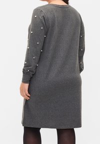 Graues Strickkleid mit langen Ärmeln, verziert mit weißen Perlenakzenten, lockerer Passform und knielangem Saum. Glatte Textur, minimalistisches Design.